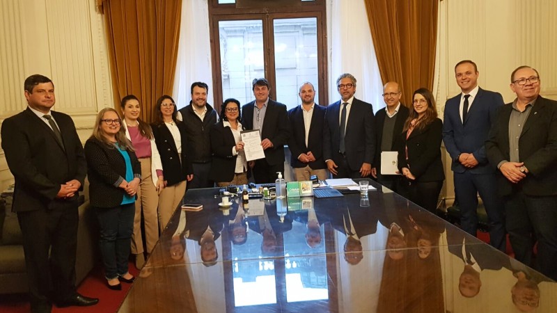 Grupo reunido, em formato de "U" em torno de mesa. Secretária Marjorie e coordenador de projeto da PGR segurando o doc de licença em foto posada.