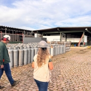 Duas pessoas utilizando capacetes de proteção caminham a céu aberto, ao lado de botijões, em vistoria da Fepam