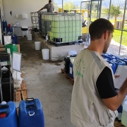 Duas pessoas realizam an&aacute;lises qu&iacute;micas. No local, diversos gal&otilde;es com produtos
